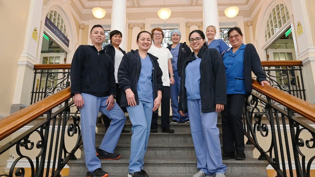 Group of female and male nurses standing on a stair case in a hospital setting smiling